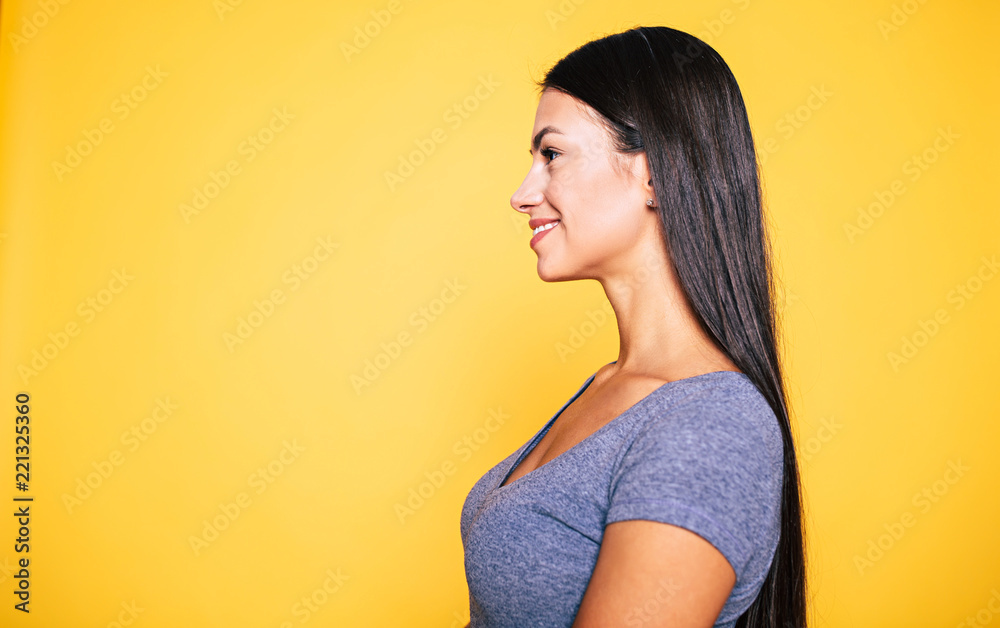 Close up Side view portrait of beautiful young smiling cute brunette woman with long healthy hair isolated on yellow background Close up Side view portrait of beautiful young smiling cute brunette woman with long healthy hair isolated on yellow background