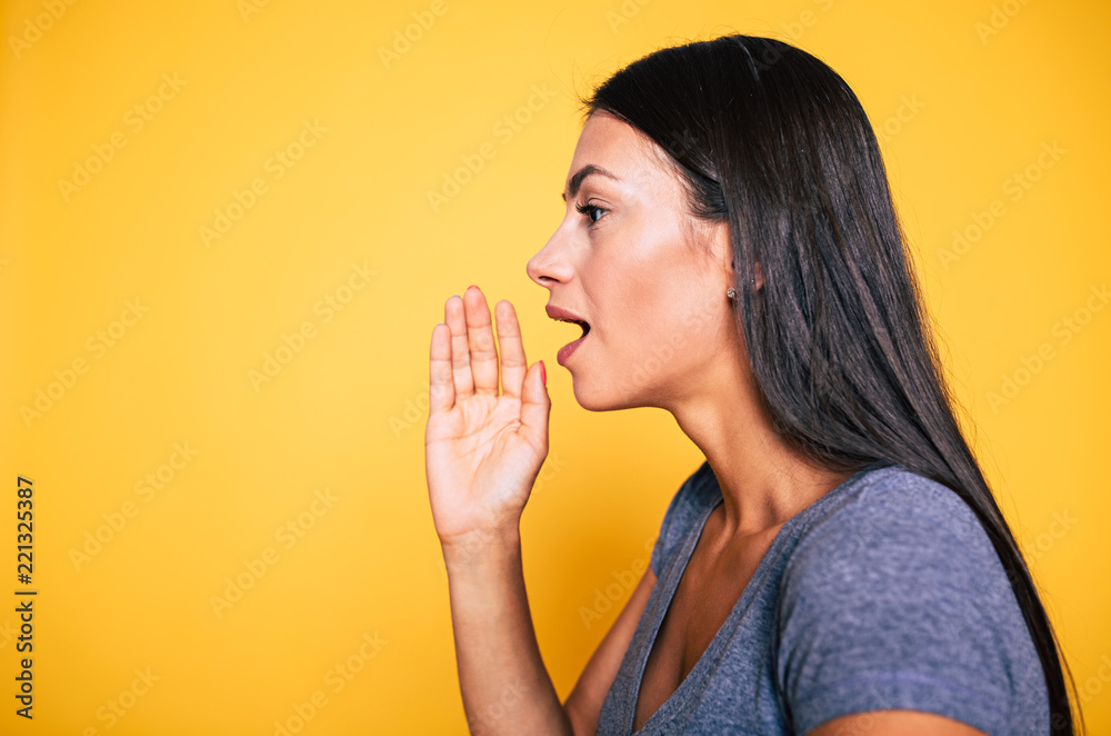 Can you hear me? Gossip and chatting. Side view portrait of cute attractive young girl, woman is shouting something away or talks for someone isolated on yellow background. Can you hear me? Gossip and chatting. Side view portrait of cute attractive young girl, woman is shouting something away or talks for someone isolated on yellow background.