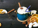 Świąteczny kubek kawy z bitą śmietaną, cynamonem, kakao, anyżem, suszonymi plastrami pomarańczy, i lukrowanymi piernikami na drewnianym tle. Ciemny retro styl z miejscem na tekst