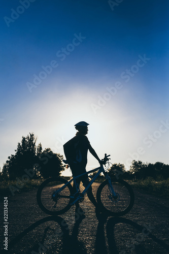Silhouette of a girl with a bicycle at sunset in the summer