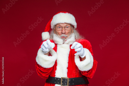 Christmas. Good Santa Claus in white gloves shows faces, grimaces, shows his tongue. Not standard behavior. Isolated on red background.