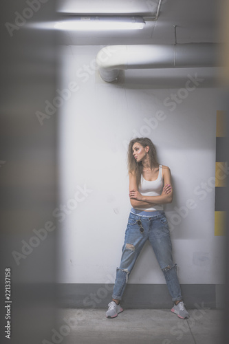 Portrait of young beautiful woman wearing white tank shirt and blue jeans with long hair at underground garage