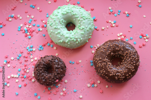 Colorful donuts in the glaze on the pink background with multi-colored sprinkles sugar stars. Can be used as a background for birthday or other holidayn