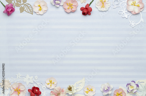 Paper colored flowers on the edges  blue background with stripes and blank space in the center. Top view