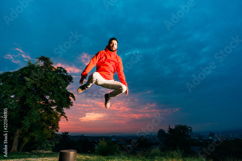 Young Caucasian man performs parkour jumping. Young parkour man jumping in park on a sunrise against a blue sky