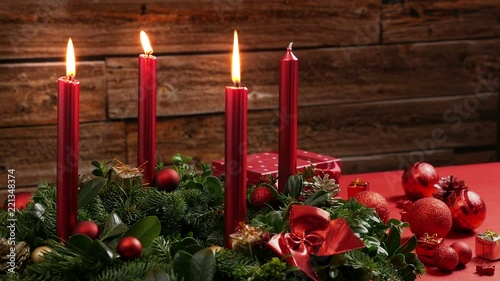 Three burning red candles on a traditional advent wreath of green fir twigs and mistletoes with festive decoration in front of a rustic wooden wall, close-up real time shot with copy space, nobody