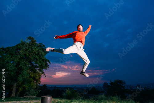 Man who does parkour in city park. Young parkour man jumping in park on a sunrise against a blue sky