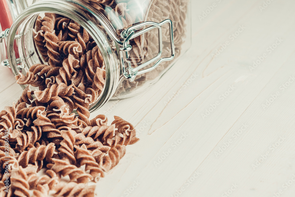 Macaroni fusilli takes off from a glass jar on a white wooden table
