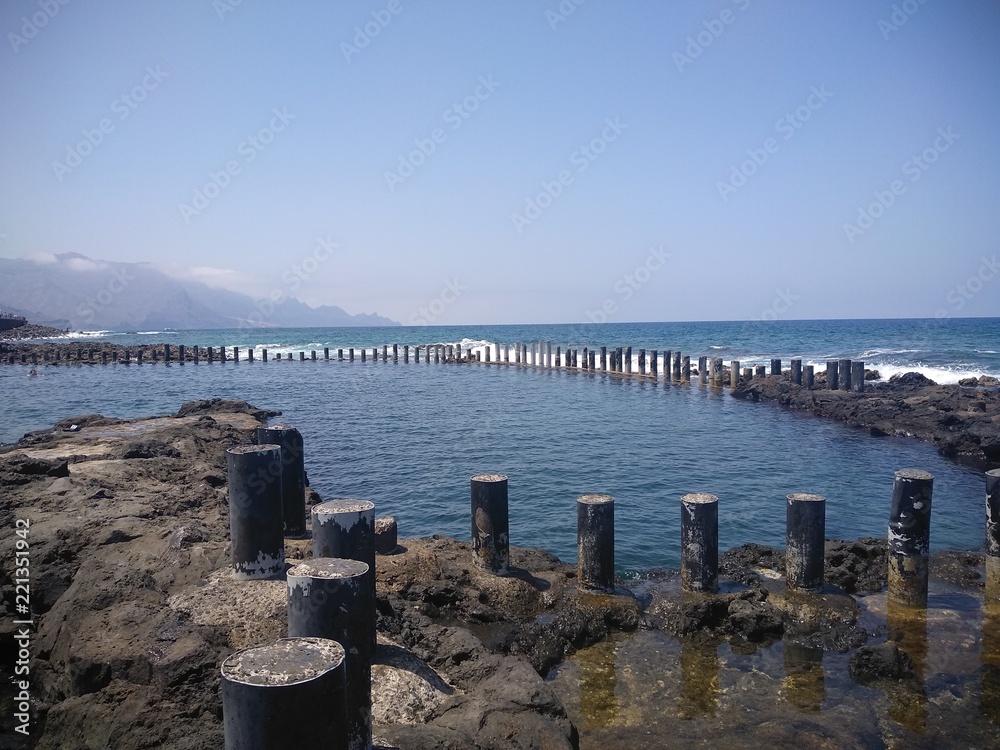 piscina natural de agua marina en la costa cercada por pequeños postes de hormigon