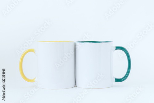 Two white mugs, with a green and yellow handle on a light background. 