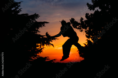 Man silhouette doing parkour activity on sunset. Silhouette of young parkour man while jumping and flipping upside down in park on a sunrise