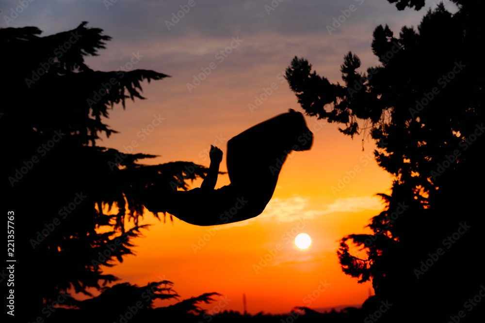 Silhouette of young parkour man while jumping and flipping upside down in park on a sunrise