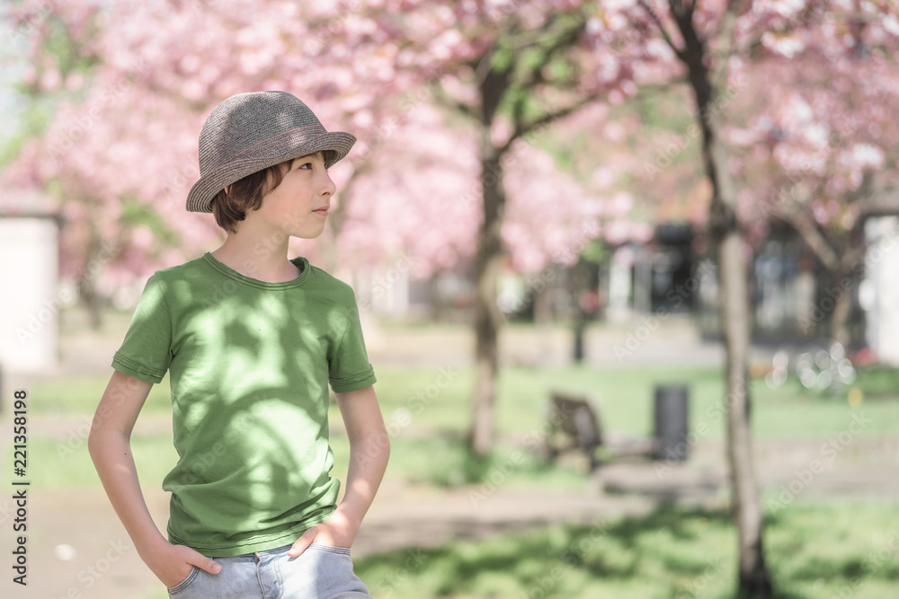 Portrait of a boy in a T-shirt and hat standing against a background of flowering trees.