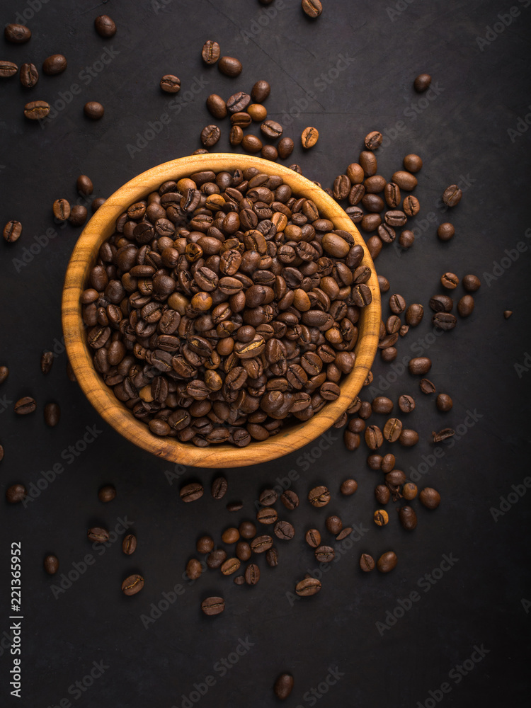 Fresh roasted coffee beans in a wooden bowl on a black stone background top view with copy space. Fresh roasted coffee beans in a wooden bowl on a black stone background top view with copy space.