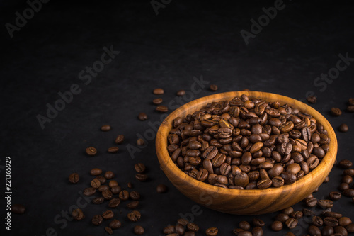Fresh fried coffee beans in a wooden bowl on a black stone background with space for your text.