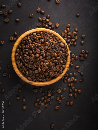 Fresh roasted coffee beans in a wooden bowl on a black stone background top view with copy space.
