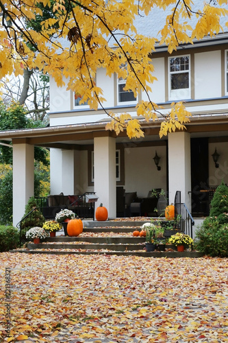 Seasonal house outdoor decoration. Main entrance stair and porch of the stylish house decorated for autumn holidays season, branches of the yellow colored tree and foliage on a foreground.
