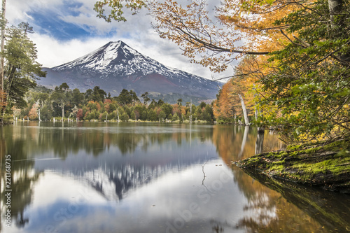 Captren Lagoon during Autumn Season, a colorful mirror over the waters with amazing reflections of Llaima Volcano full of colors with the trees foliage fallen inside Conguillio National Park, Chile photo