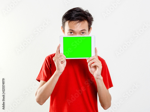 Young man shows green screen blank tablet while wearing red shirt short sleeve on white background.