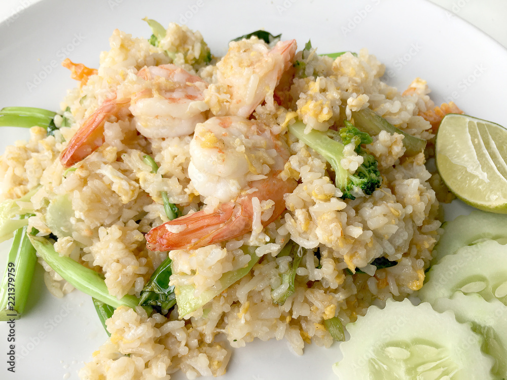 Fried rice with prawn herbs and vegetables served with lemon and cucumber in white plate on white background. Part of a series of nine Asian food dishes. Thai Food. Fried rice with prawn herbs and vegetables served with lemon and cucumber in white plate on white background. Part of a series of nine Asian food dishes. Thai Food.