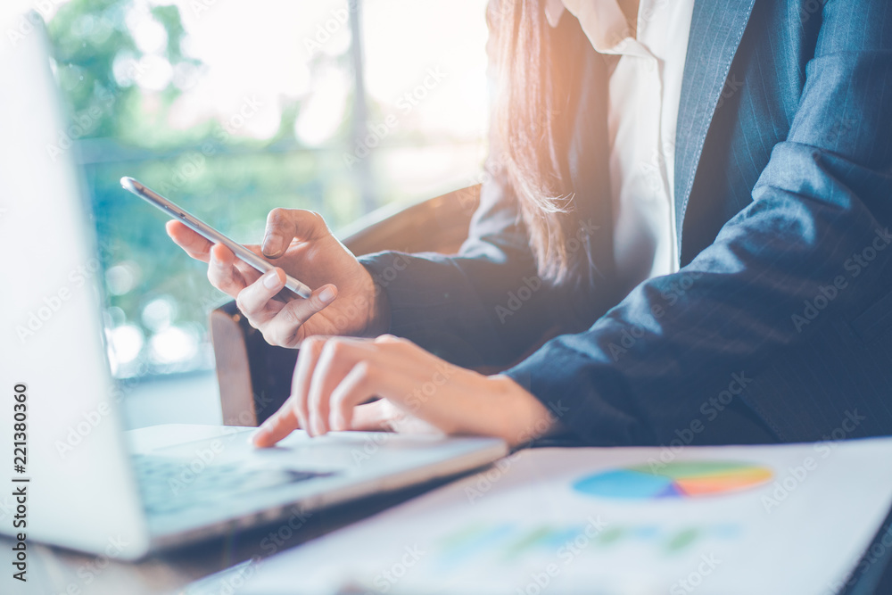 Business woman hand uses a phone to work on charts and graphs that show results.
