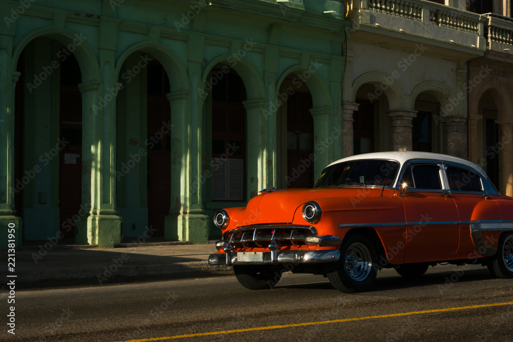  El auto antiguo de color naranja pasa cerca de los edificios viejos.