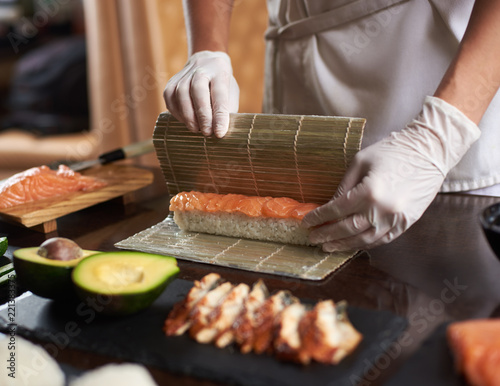 Close up view of process of preparing rolling sushi with disposable gloves on bamboo mat