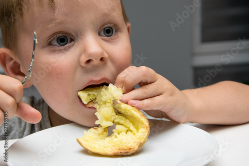A little boy eats baked potatoes.