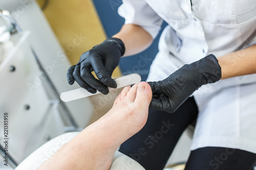 the master in black gloves in the salon makes manicure pedicure to the client