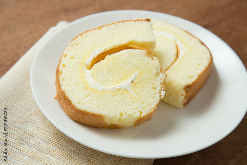 Slices of vanilla roll cake in white plate on wooden table.