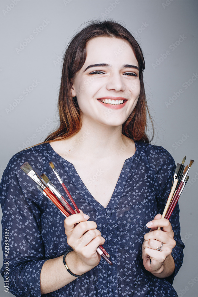 Close up portrait of pretty smiling woman with paintbrushes isolated on grey background. Artist. Art concept. Pain brush Close up portrait of pretty smiling woman with paintbrushes isolated on grey background. Artist. Art concept. Pain brush