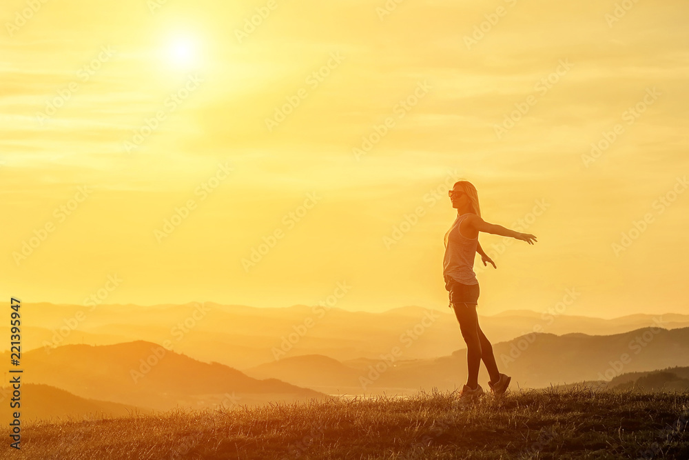 Happy woman with open arms stay on the peak of the mountain beautiful sunset background