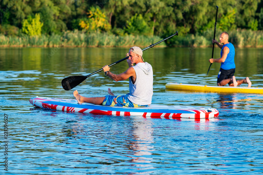Happy friends relax on a SUP boards on large river