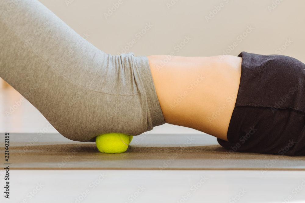 Close up of female doing self-massage technique applying tennis balls for back pain relief, working out on fitness mat on grey studio floor background, closeup. - obrazy, fototapety, plakaty 