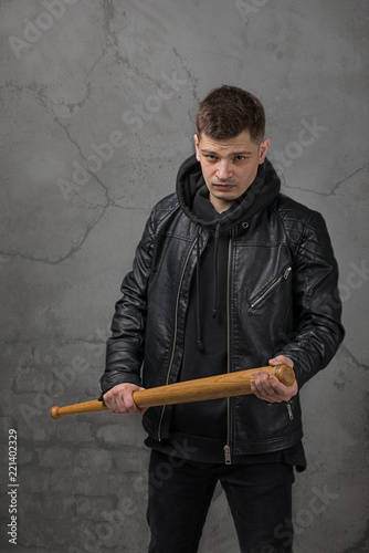 The young gue wearing leather jacket on a black wall in fighting pose with baseball bat