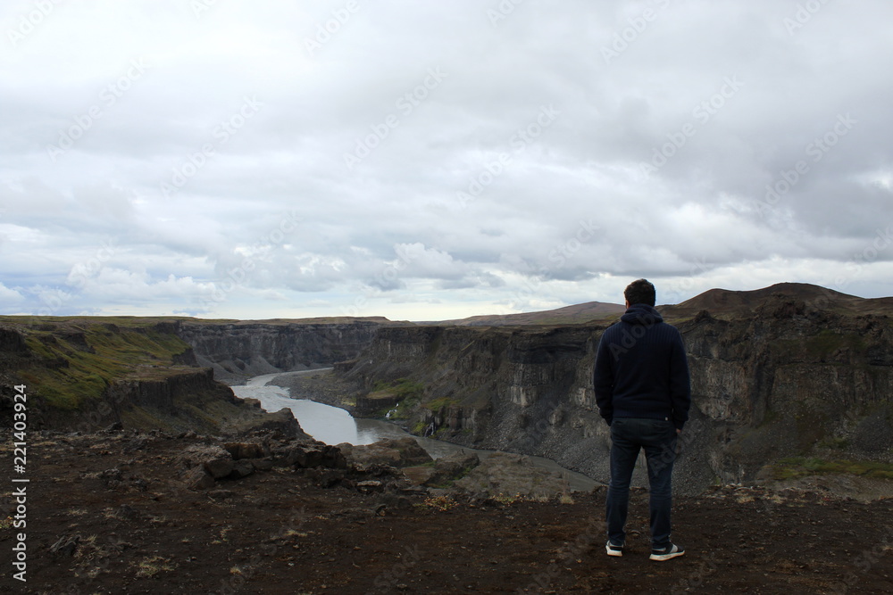 Man standing and overlooking a waterfall canyon in Iceland