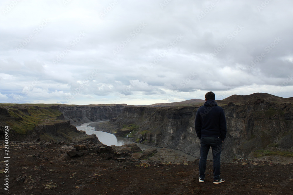 Man standing and overlooking a waterfall canyon in Iceland Man standing and overlooking a waterfall canyon in Iceland