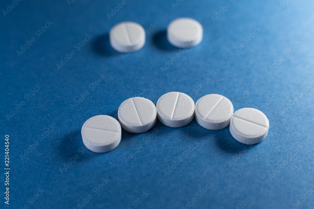 Sad smile made from white pills on blue background Sad smile made from white pills on blue background