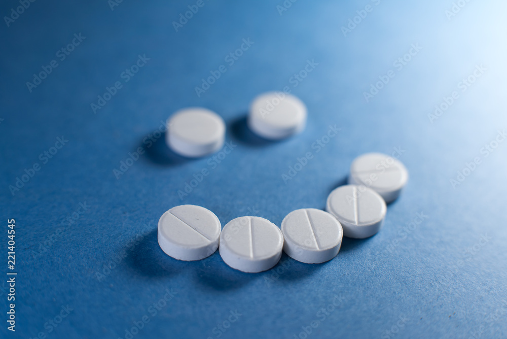 Happy smile made from white pills on blue background Happy smile made from white pills on blue background
