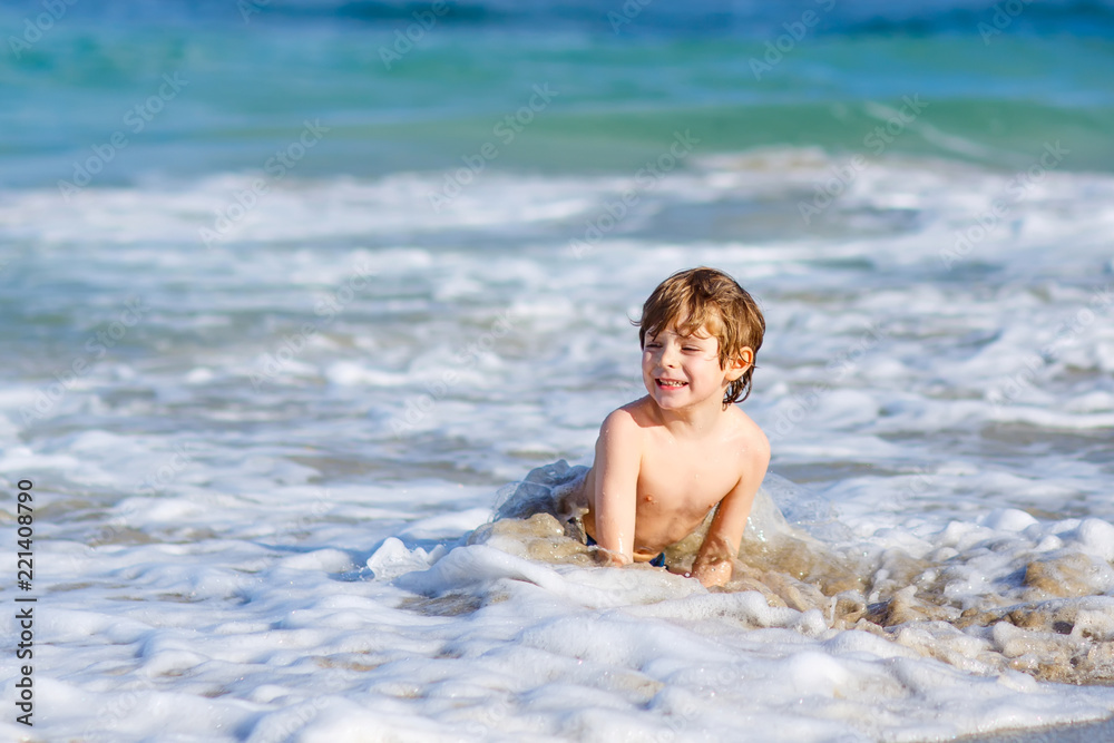 Adorable little blond kid boy having fun on ocean beach. Excited child playing with waves, swimming, splashing and happy about family vacations in Miami, Florida, USA Adorable little blond kid boy having fun on ocean beach. Excited child playing with waves, swimming, splashing and happy about family vacations in Miami, Florida, USA