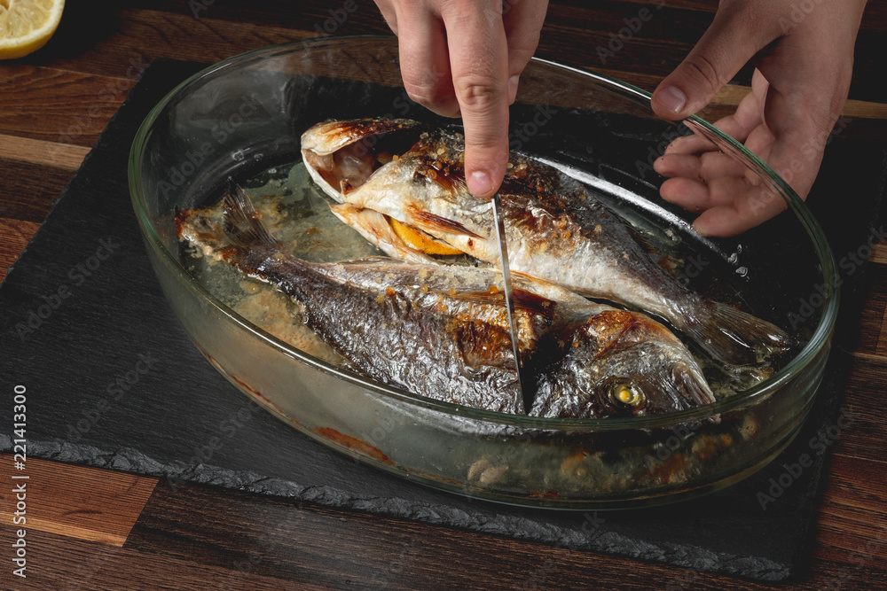 Baked sea fish with seasoning in baking pan on wooden table background.