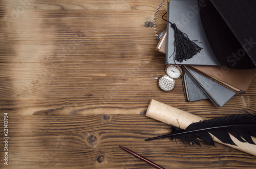 Graduate cap, pocket watch, stack of books, feather pen and scroll diploma on the wooden school desk with copy space.