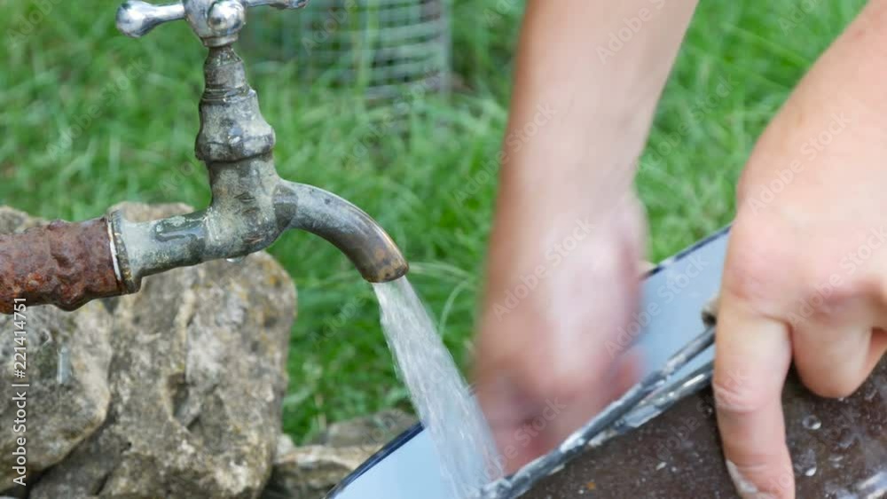 Man washes a bucket under the tap faucet outdoors Man washes a bucket under the tap faucet outdoors