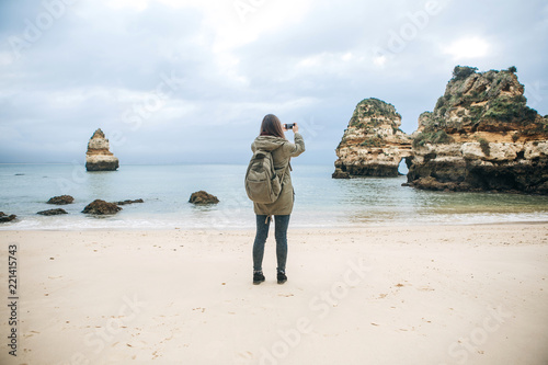 Girl tourist with a backpack photographing a beautiful landscape standing on the Atlantic coast.