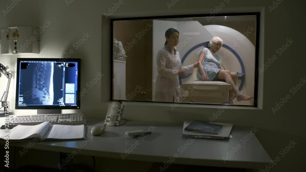 Panning shot of female doctor helping senior woman to leave patient table in MRI room after examination Panning shot of female doctor helping senior woman to leave patient table in MRI room after examination
