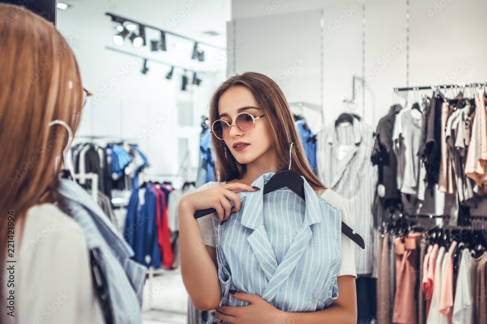 happy woman choosing clothes and looking to mirror in mall or clothing store happy woman choosing clothes and looking to mirror in mall or clothing store