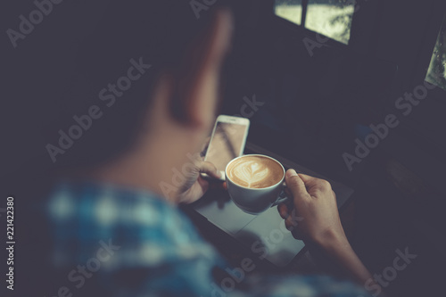 Young man drinking coffee cup in cafe and looking at phone screen, over shoulder rear view. vintage toned. © NopponPAT