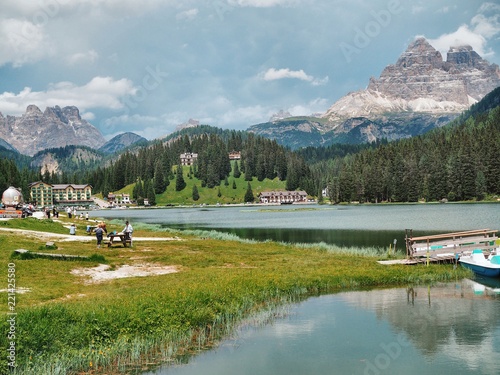 A picturesque panorama in the Dolomites. There are huge mountains covered with snow, coniferous forests, mountain clear azure lake, wild deserted place