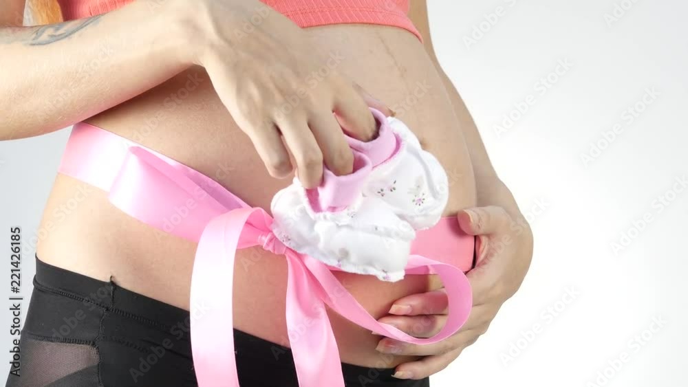 Pregnant mummy in underwear playing with baby booties. belly with pink ribbon. slow motion Pregnant mummy in underwear playing with baby booties. belly with pink ribbon. slow motion