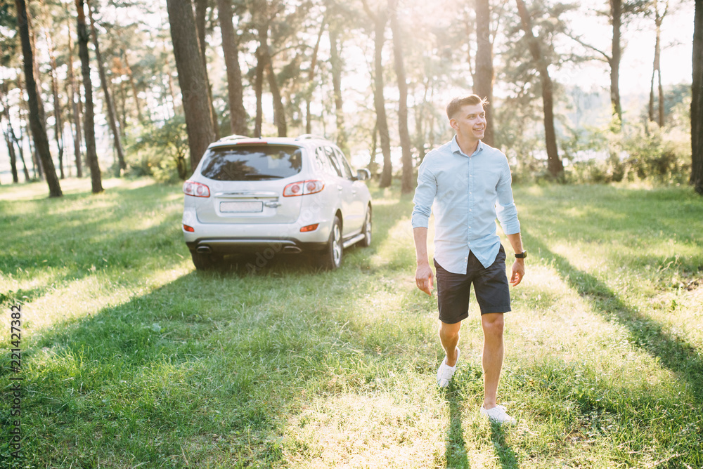 A man of a pretty appearance looks in the middle of a forest near his white car